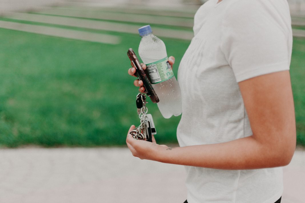 woman carrying disposable water bottle with phone and keys