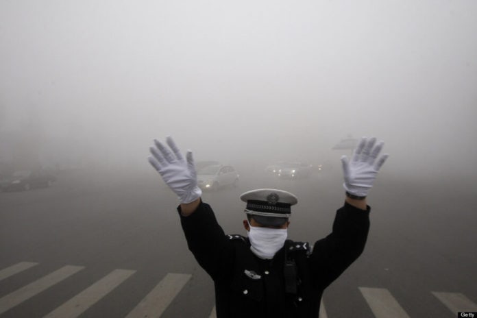 A policeman gestures as he works on a street in heavy smog in Harbin, northeast China's Heilongjiang province, on October 21, 2013. Choking clouds of pollution blanketed Harbin, which is famed for its annual ice festival, reports said, cutting visibility to 10 metres (33 feet) and underscoring the nation's environmental challenges. CHINA OUT AFP PHOTO (Photo credit should read STR/AFP/Getty Images)