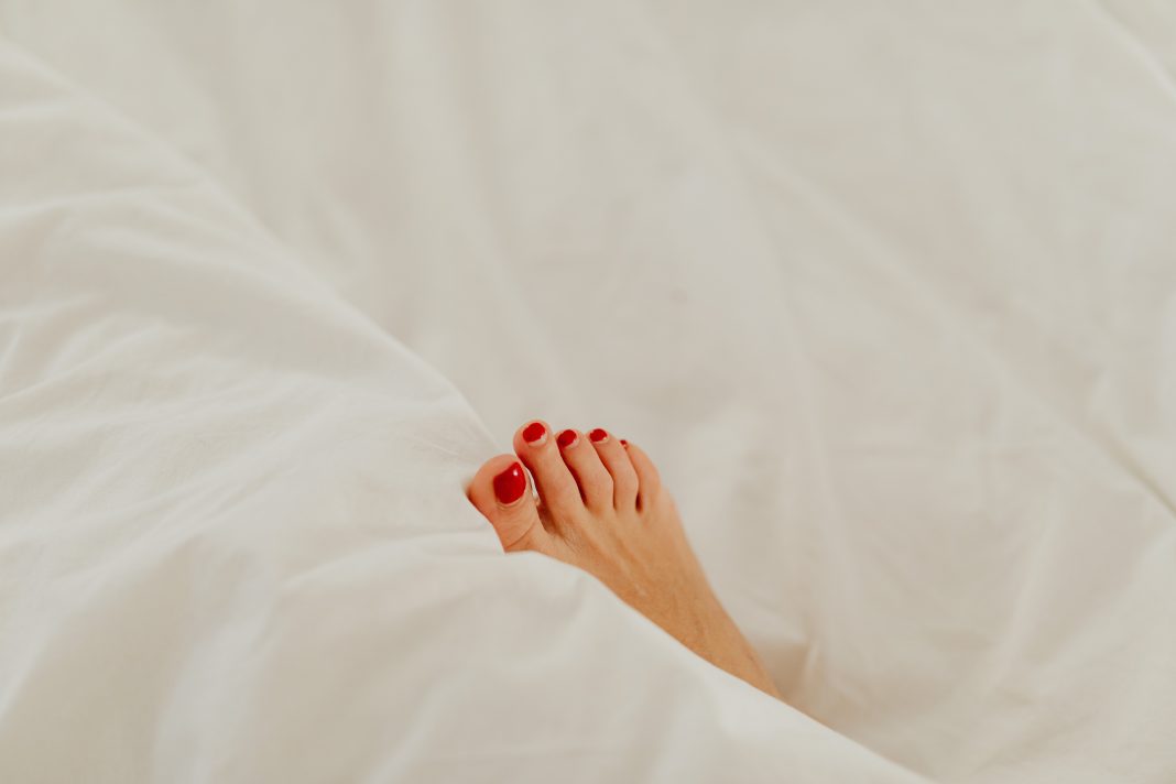 foot with red nail polish on white bedsheets