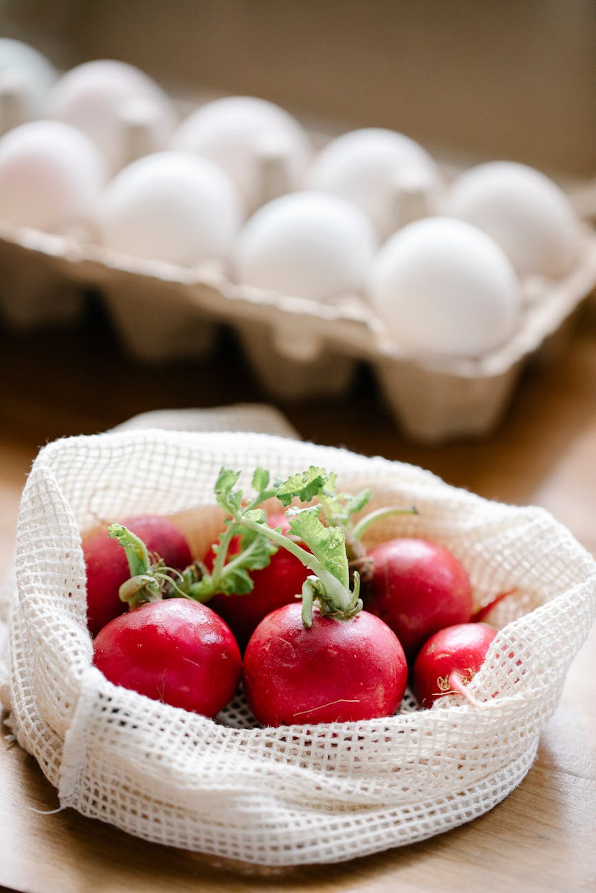 ripe radishes placed on table near white eggs in box
