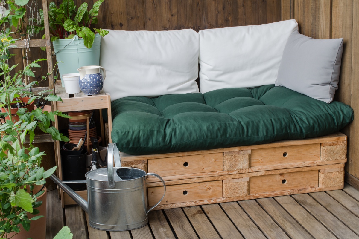A small porch seating area made from reclaimed wood pallets features pillows, potted plants, and a small side table.