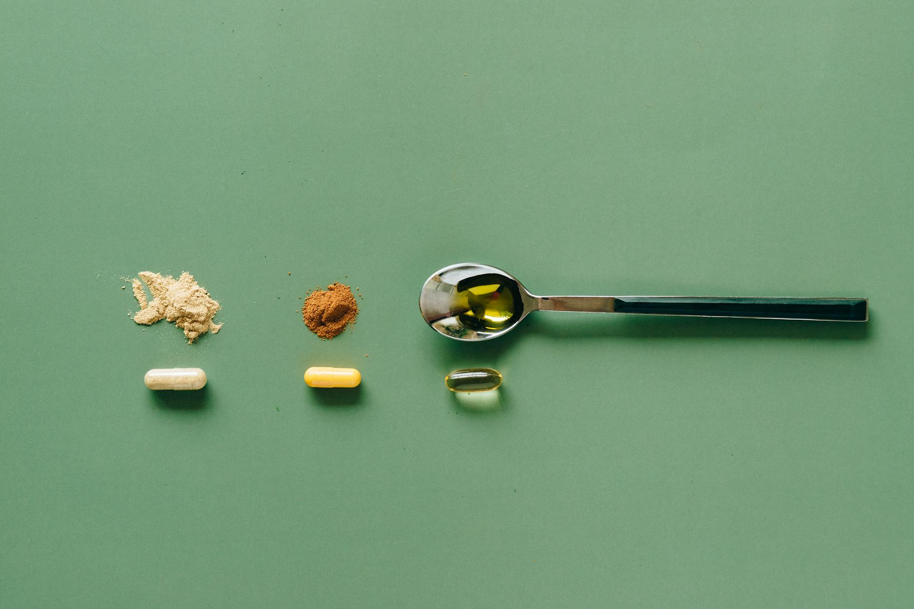 stainless steel teaspoon beside brown powder and capsules